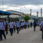 Ilustrasi buruh pabrik di kawasan industri yang menghadapi tekanan ekonomi dan ketidakpastian kerja.