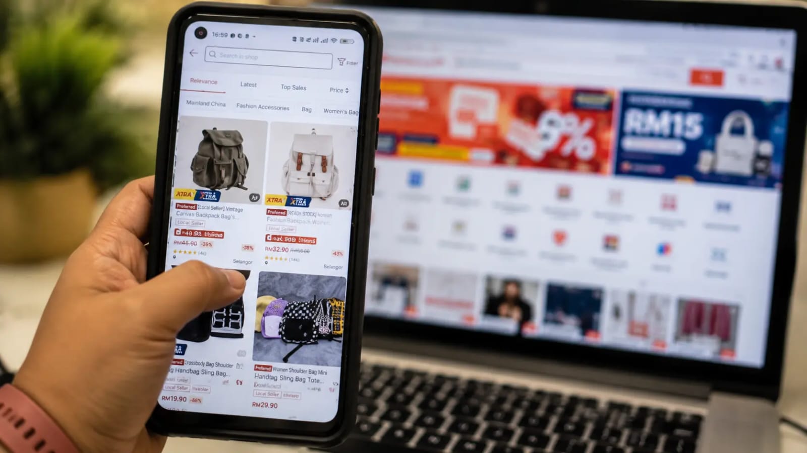 Pelaku UMKM menggunakan smartphone untuk mengelola penjualan di marketplace dengan laptop di latar belakang.