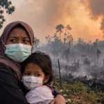 Ibu dan anak memakai masker di tengah kabut asap karhutla dan lahan yang terbakar.